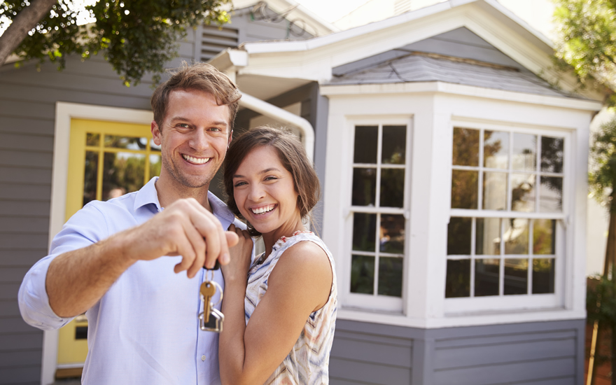 young couple holding keys up to their brand new financed home